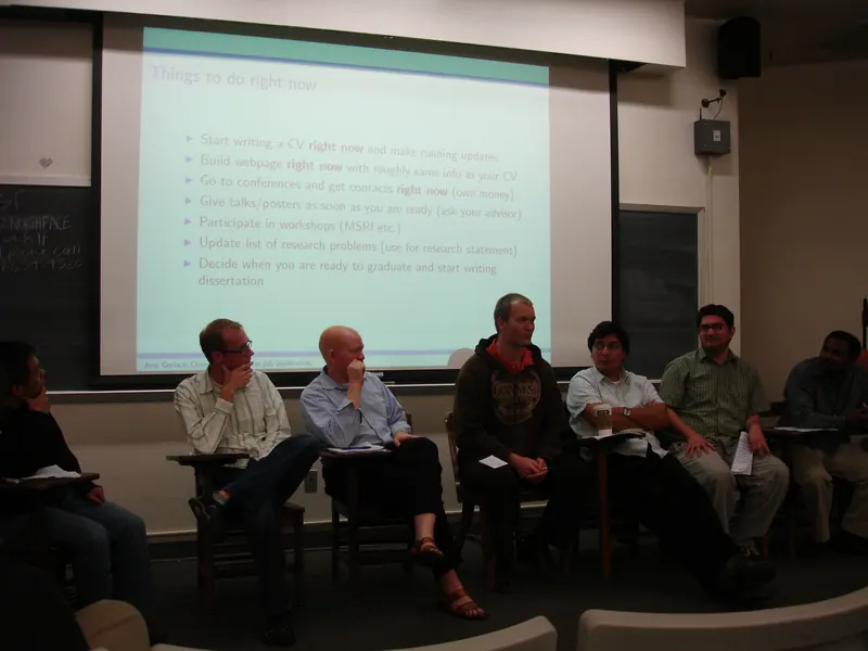 Presenters sit in front of a projector screen.