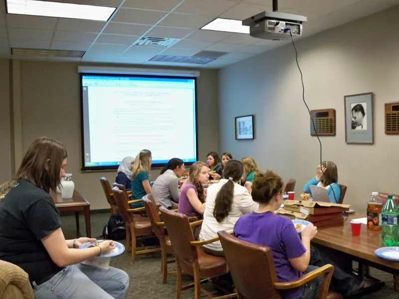 The Lounge Table is surrounded by hungry participants watching the presentation while eating pizza.