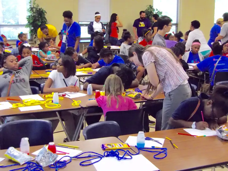 Volunteers meander the room to help the children as they explore various ways of knotting their string.