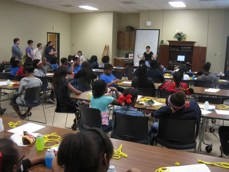 A wide shot of the room as yellow string sits in front of the children.
