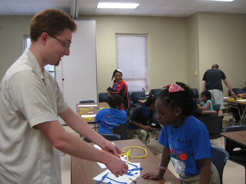 A volunteer demonstrates a particular twisting of the string to an interested participant.