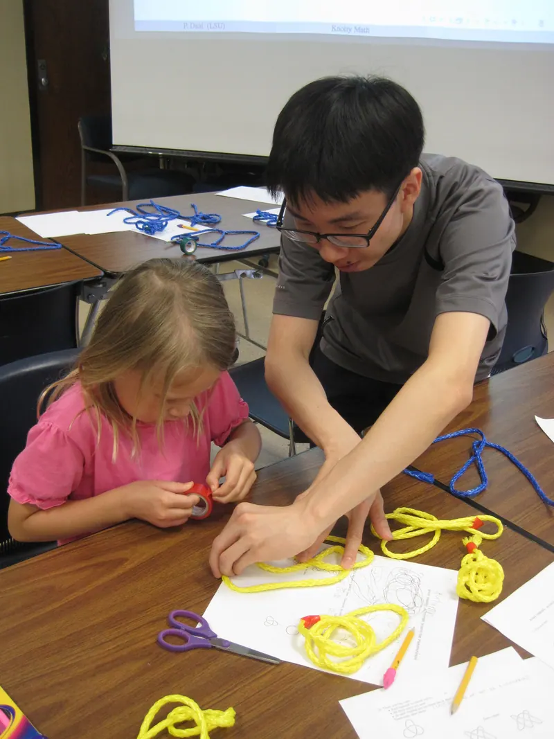 A volunteer demonstrates the crossings of a knot in a yellow string to a child.